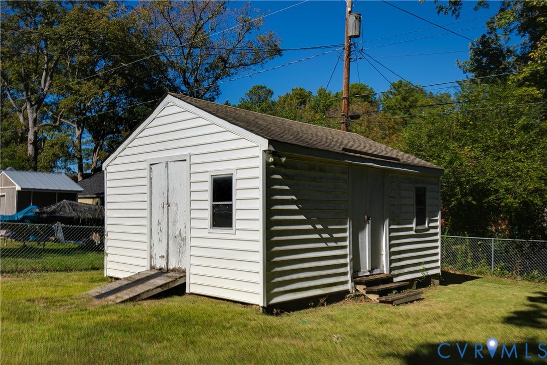 Detached storage structure featuring white horizontal siding, a gabled roof, dual entry doors, and an exterior ramp