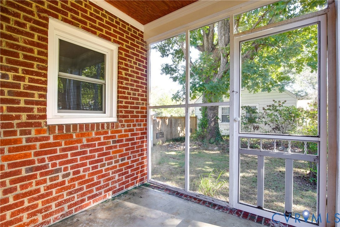 Enclosed porch featuring red brick exterior walls, wood-finish ceiling, concrete flooring, and full-height screen panels with a screened door