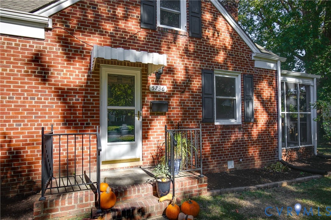 Red brick exterior featuring dark shutters, a decorative metal door canopy, and a glass-paneled storm door with metal railings
