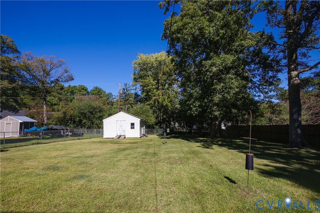 Expansive backyard featuring a level lawn, mature trees, chain-link perimeter fencing, and a detached white outbuilding