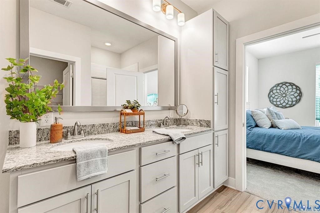 10525 Stony Bluff Drive, #107, Stony Run Condos, Ashland, VA 23005 Double vanity featuring stone countertops, integrated cabinetry with brushed hardware, a large-format mirror, and three-light glass fixture