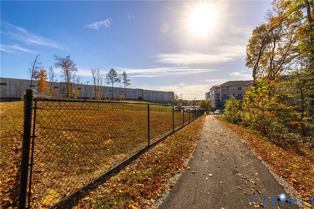 10525 Stony Bluff Drive, #107, Stony Run Condos, Ashland, VA 23005 Paved trail bordering an open grass lot enclosed by a chain-link fence, surrounded by mature trees