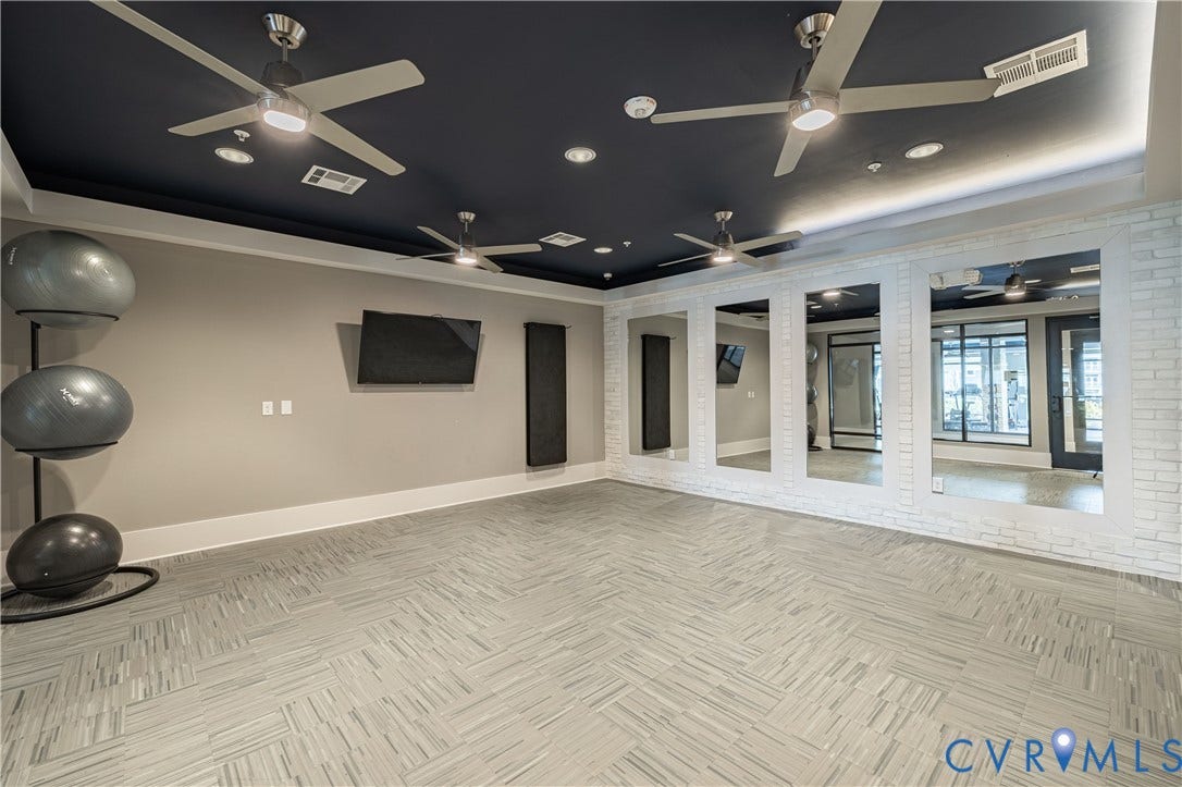 10525 Stony Bluff Drive, #107, Stony Run Condos, Ashland, VA 23005 Spacious room featuring a dark-toned tray ceiling with recessed lighting, four industrial-style ceiling fans, wall-to-wall mirrors, textured white brick accent wall, and patterned tile flooring