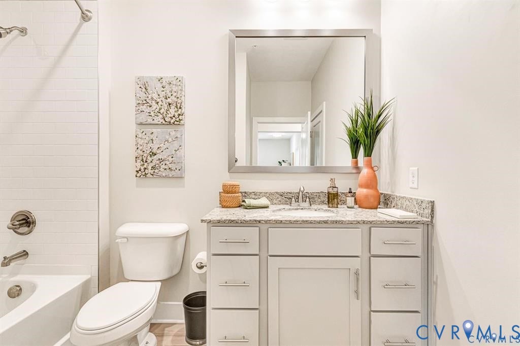 10525 Stony Bluff Drive, #107, Stony Run Condos, Ashland, VA 23005 Bathroom featuring a vanity with neutral-toned cabinetry, stone-finish countertop, undermount sink, and a large rectangular mirror, complemented by a white subway-tile shower surround