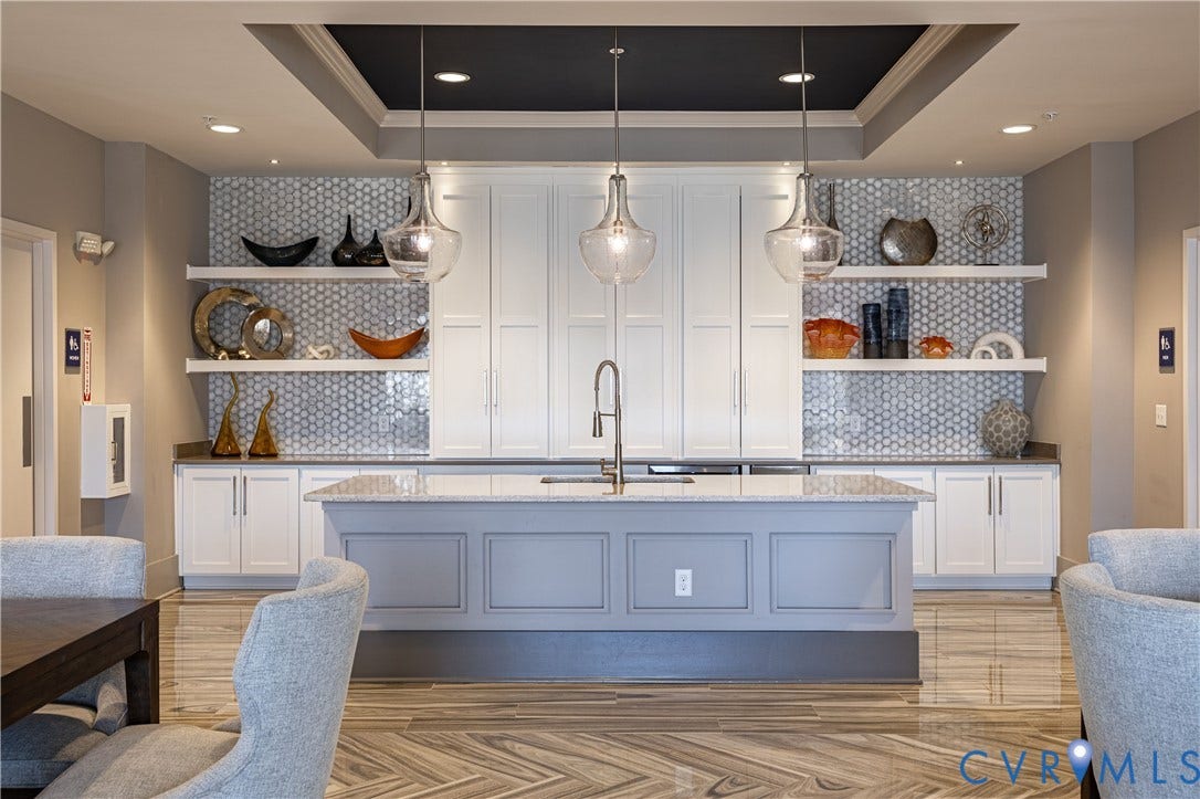 10525 Stony Bluff Drive, #107, Stony Run Condos, Ashland, VA 23005 Central island with stone countertop and undermount sink, white cabinetry with recessed-panel doors, hexagonal tile backsplash, floating wall shelving, and tray ceiling with integrated pendant lighting