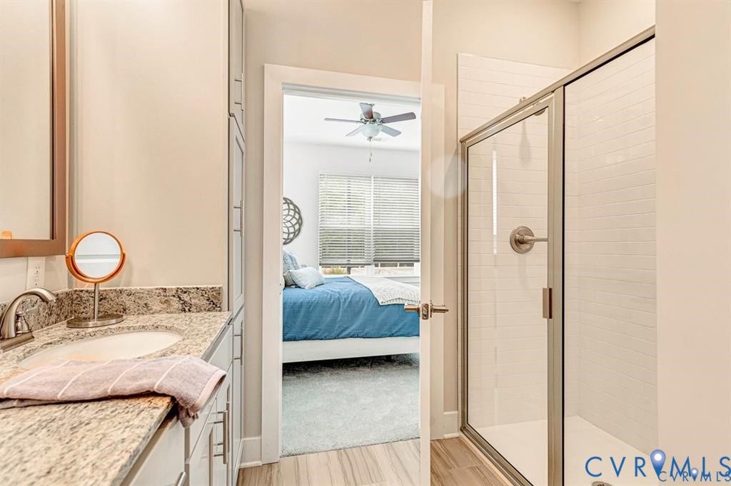 10525 Stony Bluff Drive, #107, Stony Run Condos, Ashland, VA 23005 Bathroom featuring stone-surface countertop, integrated oval sink, tall built-in cabinetry, and a glass-enclosed shower with tiled surround