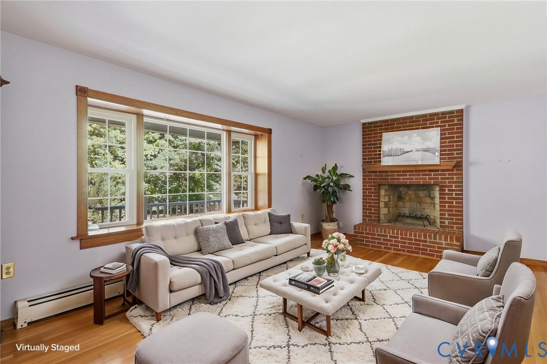 Hardwood flooring, expansive wood-framed picture window, and floor-to-ceiling brick fireplace with a wood mantel