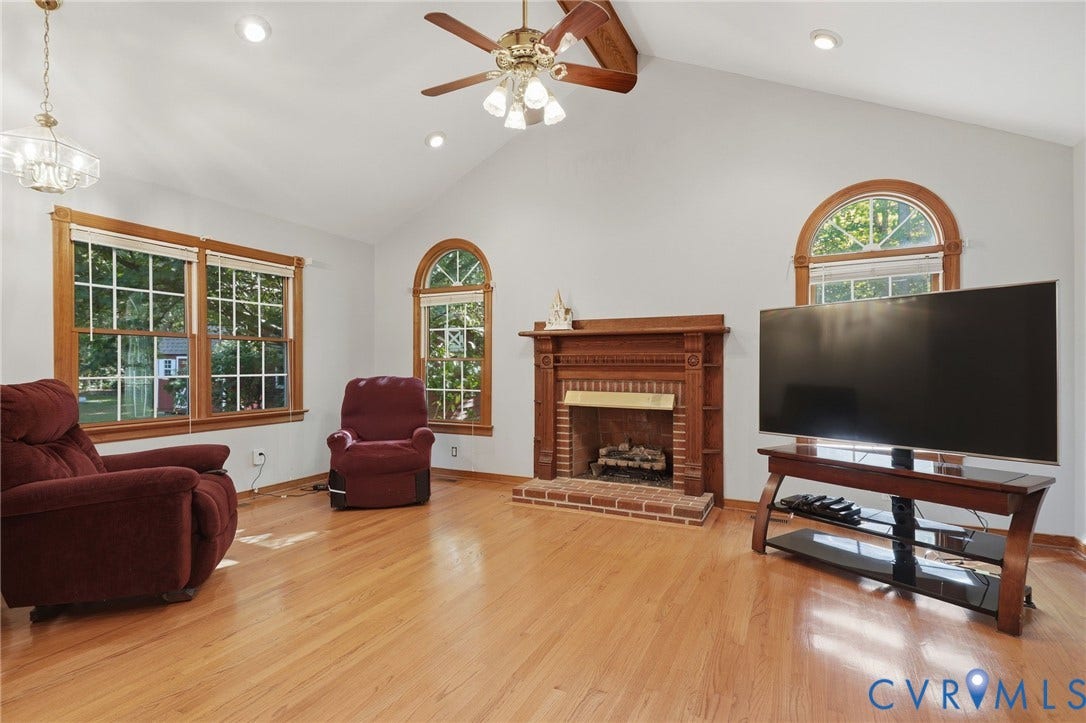 Vaulted ceiling room featuring wood-finish flooring, a brick fireplace with a wood mantel, arched windows, and recessed lighting