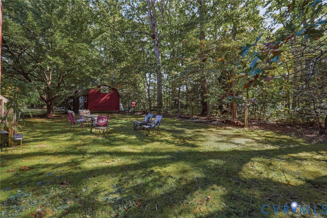 Expansive backyard featuring a level lawn, mature canopy trees, and a detached storage shed