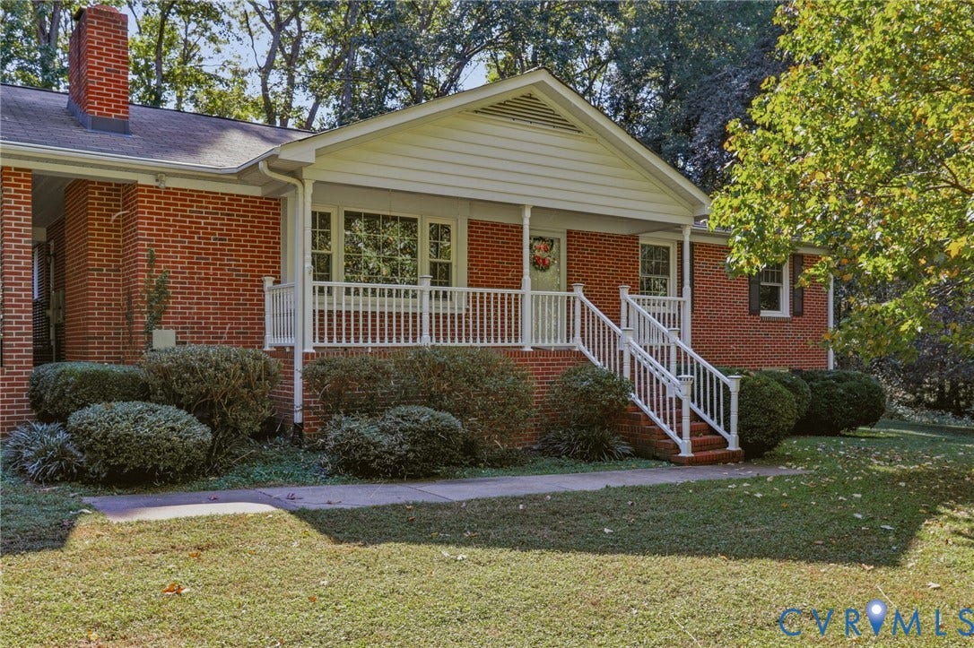 Brick exterior featuring a gabled roofline, a raised front porch with white railing, and a side-profile brick chimney