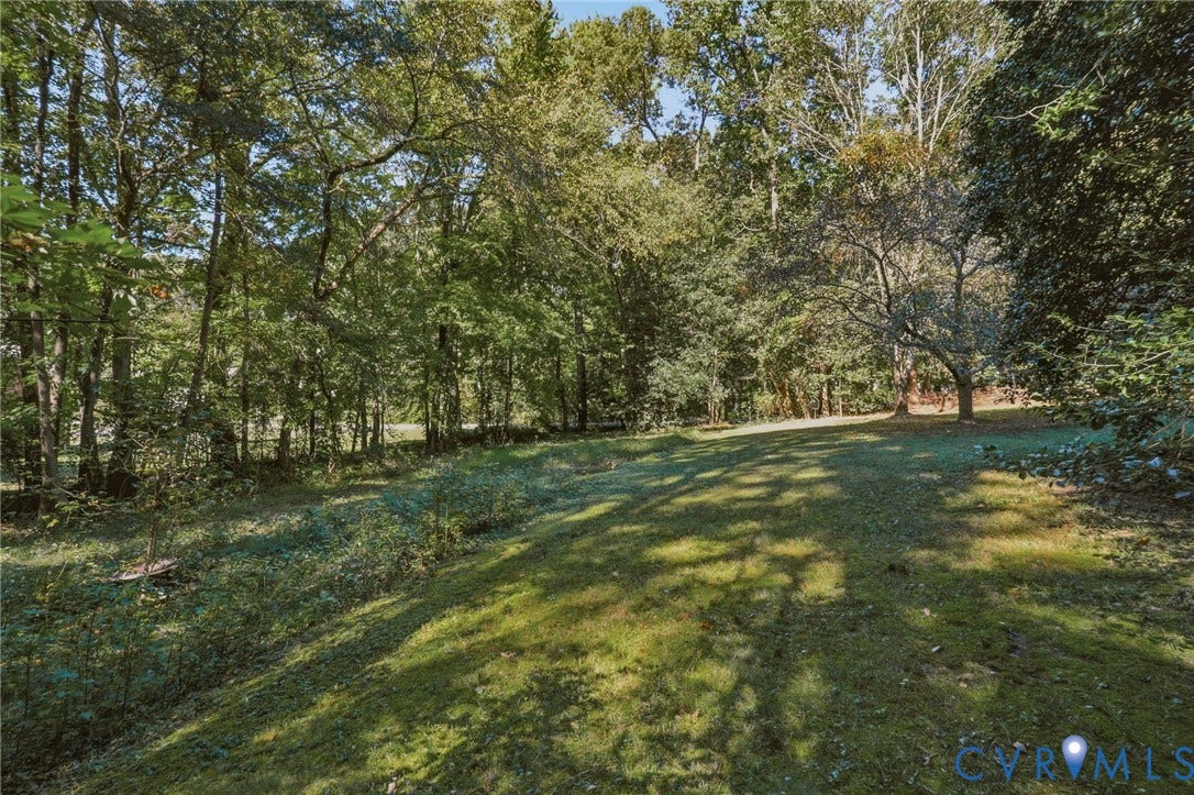 Expansive grounds featuring a grass lawn, mature trees, and natural woodland border