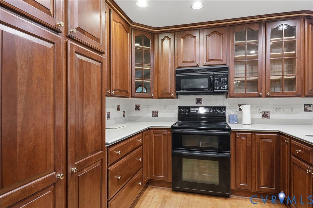 Kitchen featuring warm-toned wood cabinetry, glass-paneled upper cabinet doors, integrated black appliance suite, light-toned countertops, and wood-finish flooring
