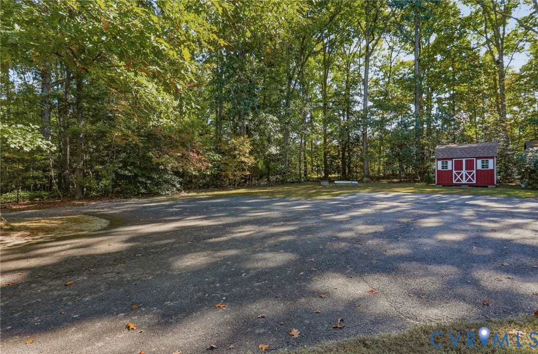 Expansive paved area featuring a standalone storage structure, bordered by mature trees and dense woodland