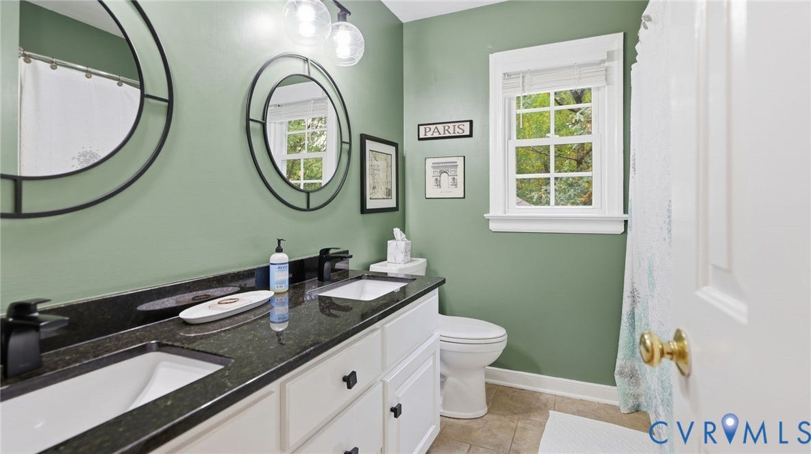 2040 Normandstone Drive, Roxshire, Midlothian, VA 23113 Dual-sink vanity with dark stone countertop, matte black fixtures, circular mirrors, and multi-pane window
