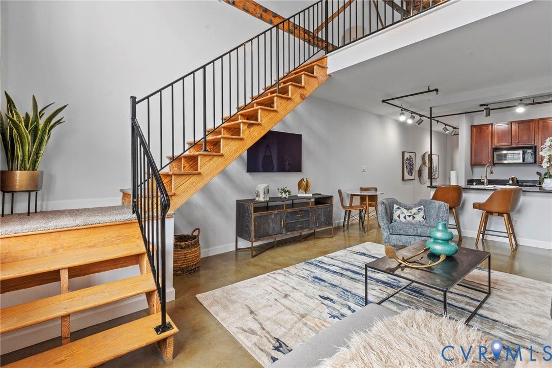 815 Porter Street, #U301, Richmond, VA 23224 Open-concept interior featuring wood-tread staircase with black metal railing, soaring vaulted ceilings, polished concrete flooring, and industrial-style track lighting