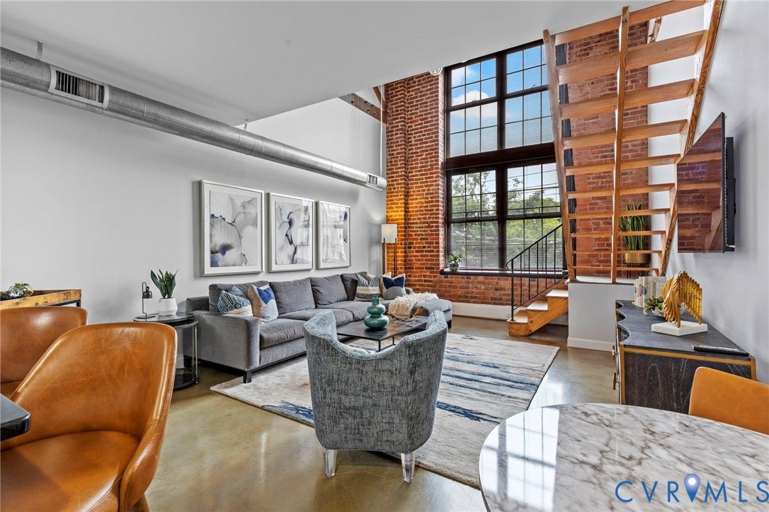 815 Porter Street, #U301, Richmond, VA 23224 Industrial-style interior featuring soaring ceilings, expansive multi-pane windows, exposed brick accent walls, polished concrete flooring, and an open-tread wooden staircase