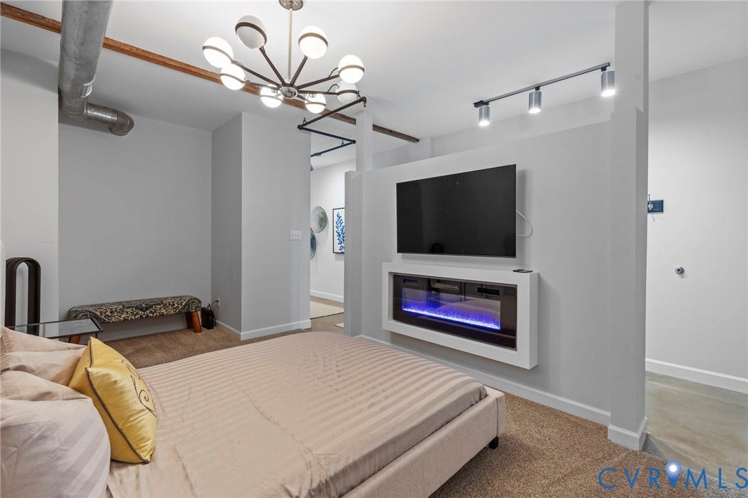 815 Porter Street, #U301, Richmond, VA 23224 Space featuring a wall-mounted electric fireplace, exposed industrial ductwork, a multi-arm statement chandelier, and adjustable track lighting