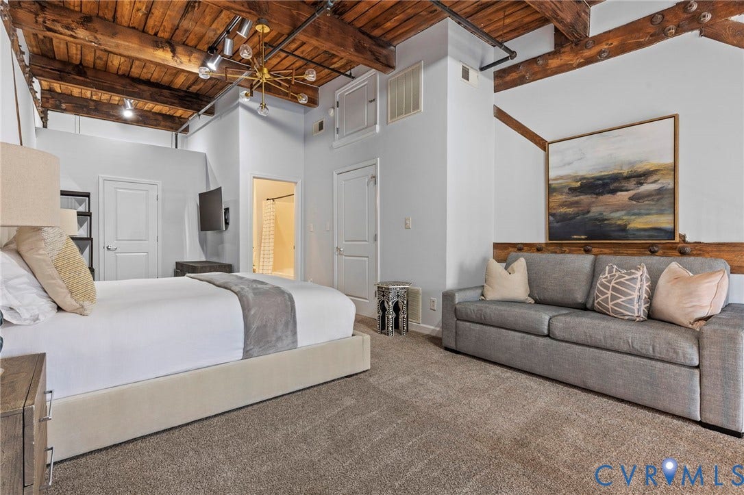 815 Porter Street, #U301, Richmond, VA 23224 Exposed timber ceiling beams, industrial-style pipe conduit, multi-arm metal chandelier, and neutral wall-to-wall carpeting