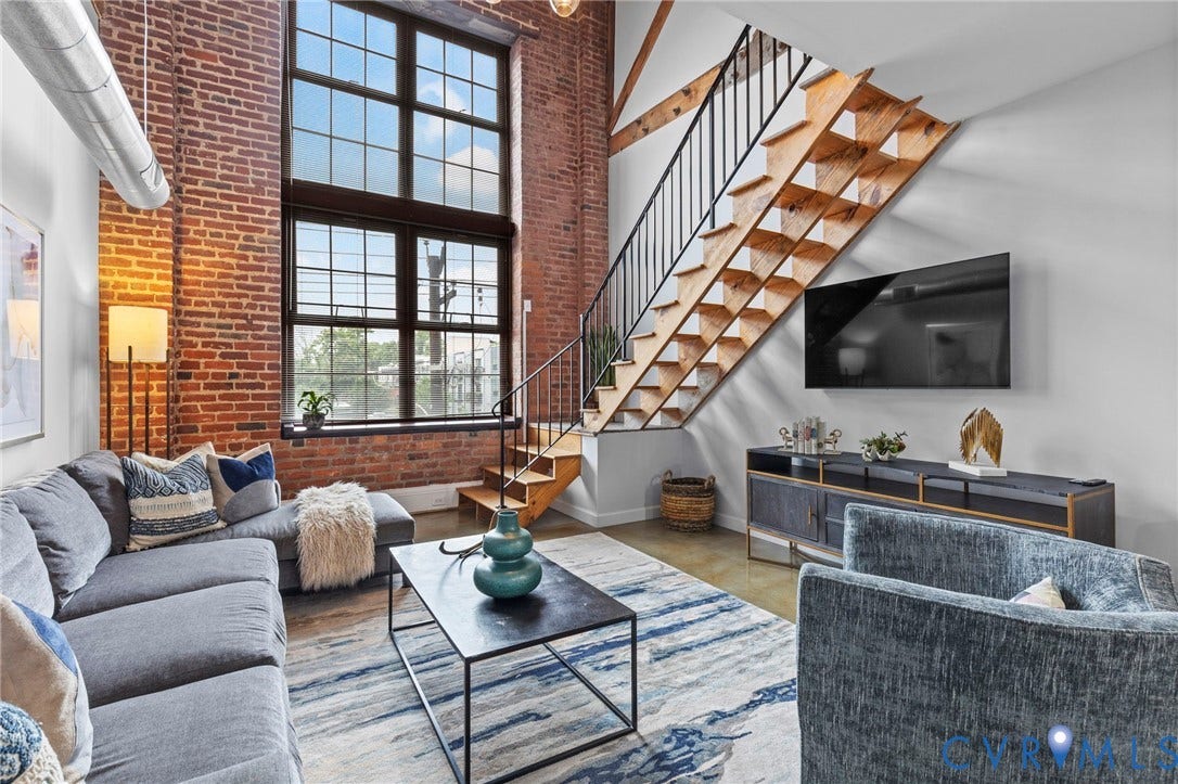 815 Porter Street, #U301, Richmond, VA 23224 Exposed brick walls, double-height industrial-style windows, open-tread wooden staircase with metal handrail, polished concrete flooring, and exposed ceiling ductwork