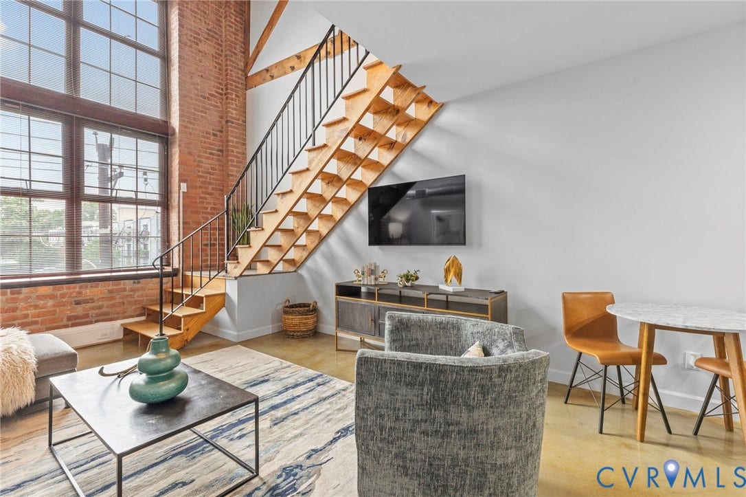 815 Porter Street, #U301, Richmond, VA 23224 Industrial-style interior featuring floor-to-ceiling multi-pane windows, exposed brick wall, open-riser staircase with metal railing, and concrete flooring