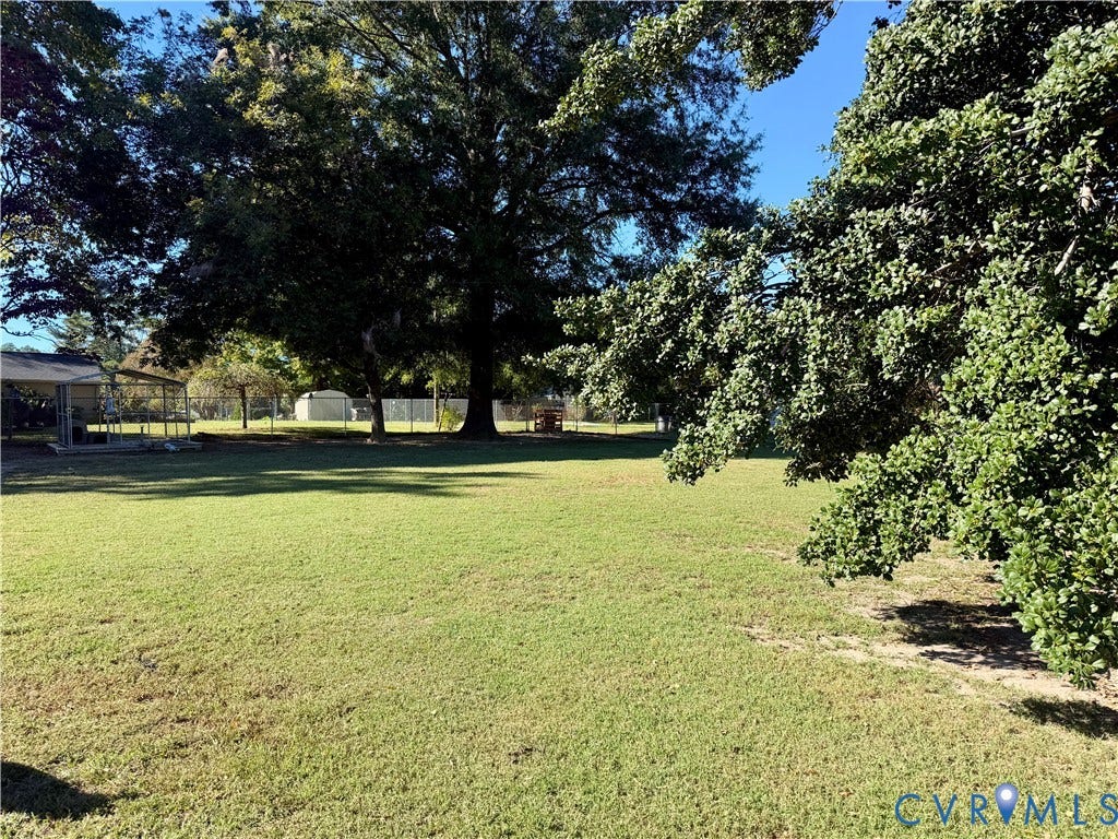 Expansive backyard featuring a large grass lawn, mature trees, a metal-framed structure, and perimeter fencing