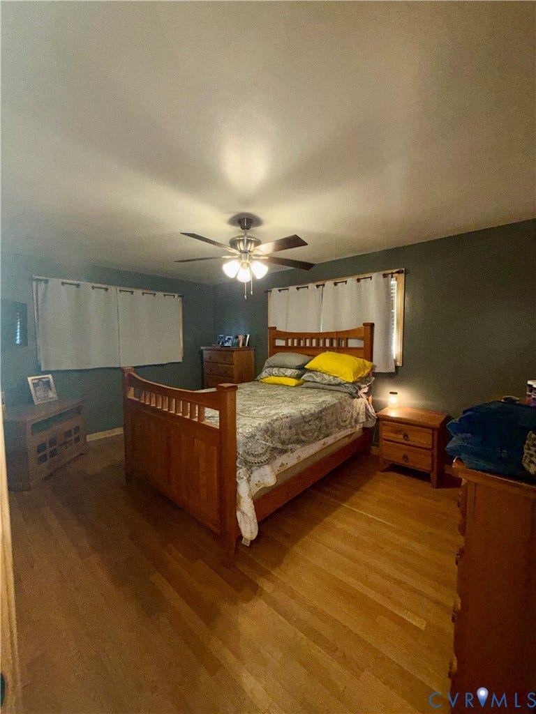 Room featuring wood-finish flooring, a ceiling fan with integrated lighting, and dual windows