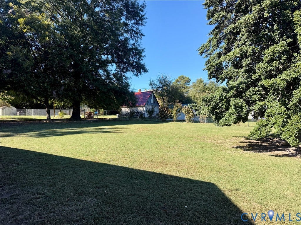 Expansive backyard featuring a large grass lawn, mature trees, and perimeter fencing