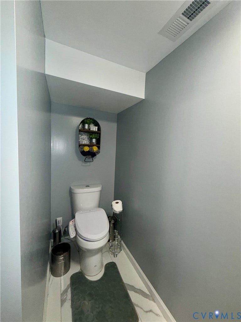 Enclosed space featuring white stone-finish floor tiling, neutral wall paint, and a two-piece white porcelain toilet