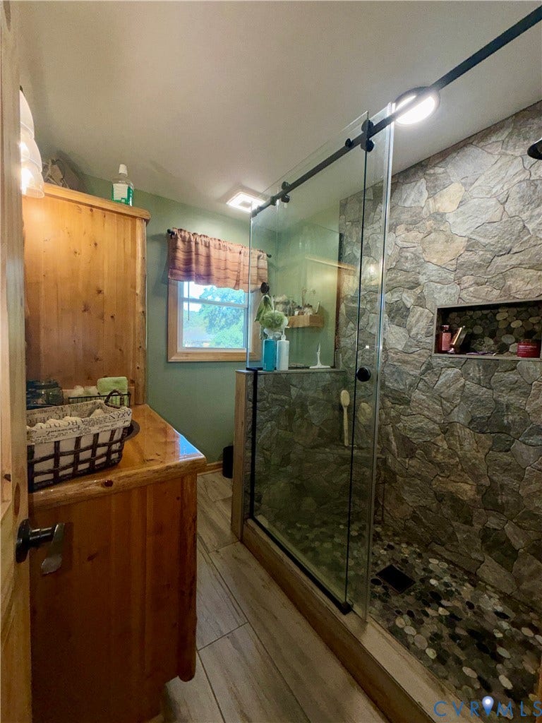 Walk-in shower with a sliding glass door, river rock flooring, and natural stone surround