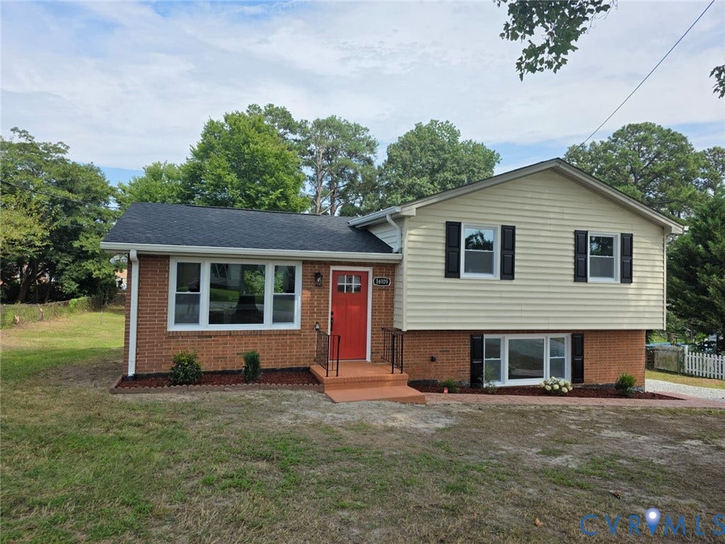 Split-level exterior featuring a combination brick and horizontal siding facade, asphalt shingle roof, dark decorative shutters, and a prominent red front door