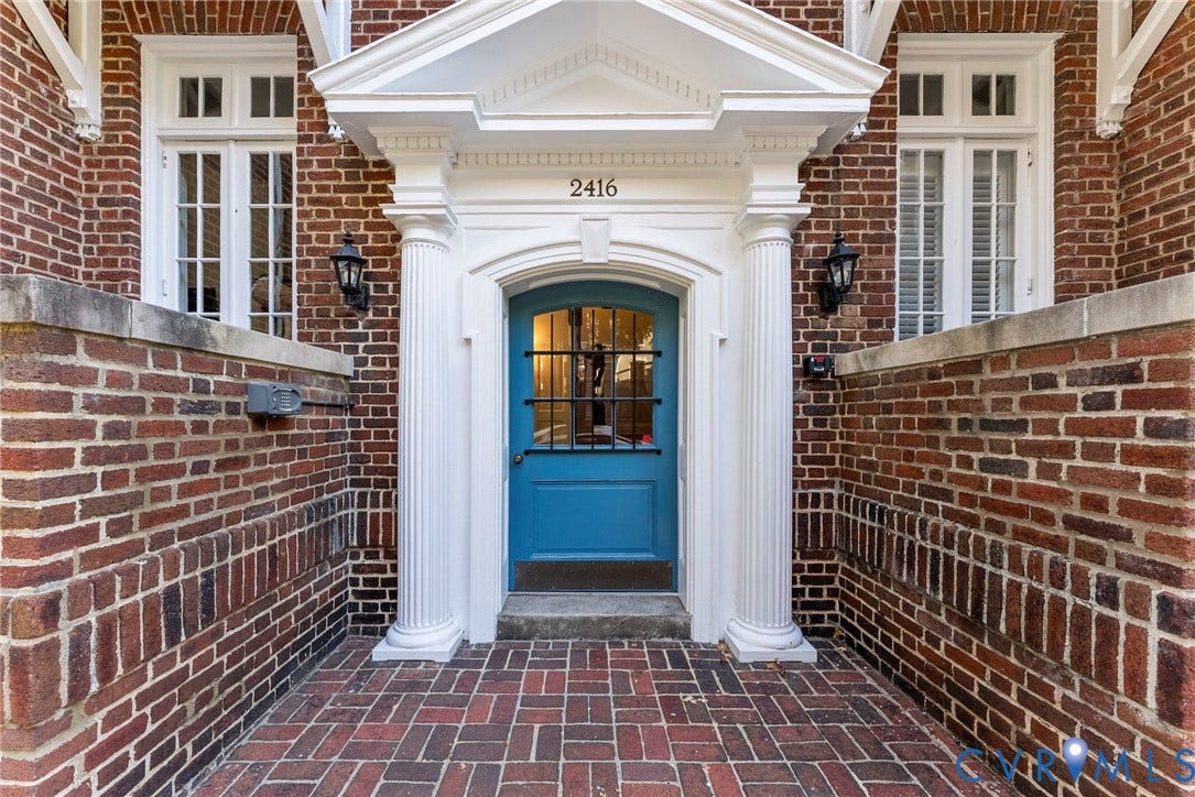 2416 Park Avenue, #U4, The Fan District, Richmond, VA 23220 Red brick exterior featuring a classical pedimented entryway, fluted columns, a blue wood-panel door with an iron grille, and a brick-paved stoop