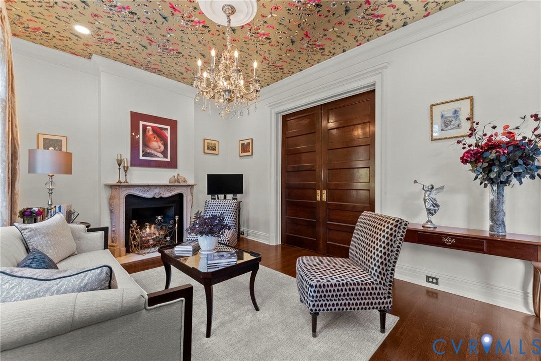 2416 Park Avenue, #U4, The Fan District, Richmond, VA 23220 Interior space featuring wood-finish flooring, a decorative fireplace with carved stone surround, a central crystal chandelier with ceiling medallion, patterned wallpapered ceiling, and solid wood double doors