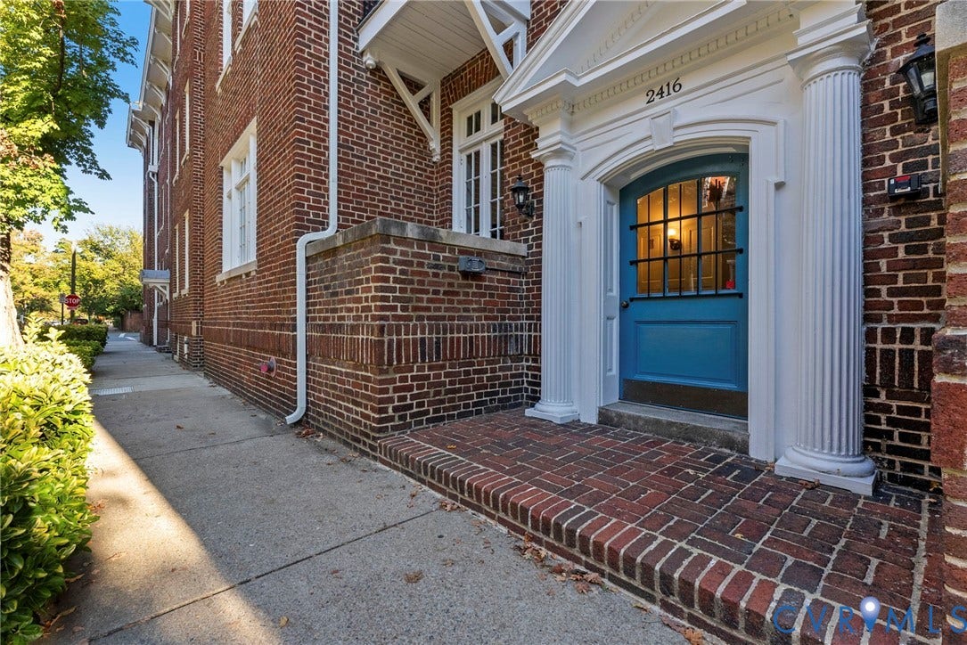 2416 Park Avenue, #U4, The Fan District, Richmond, VA 23220 Brick exterior facade featuring a pedimented entryway with fluted columns, a blue-painted door with an iron grille window, and a brick porch