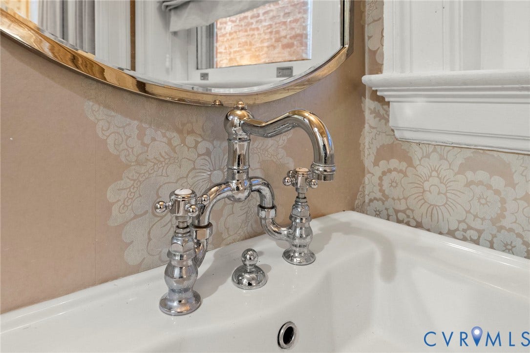 2416 Park Avenue, #U4, The Fan District, Richmond, VA 23220 Polished chrome bridge-style faucet with cross-handle controls, white porcelain sink, and oval wall mirror with metallic frame