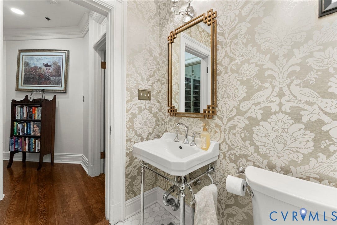 2416 Park Avenue, #U4, The Fan District, Richmond, VA 23220 Powder room featuring patterned wallpaper, a wall-mounted brass-finish mirror, a white console sink with chrome legs, and hexagonal tile flooring