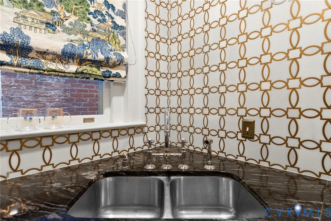 2416 Park Avenue, #U4, The Fan District, Richmond, VA 23220 Double-basin stainless steel sink with a polished metal bridge-style faucet and side sprayer, set into a dark natural-stone countertop with integrated backsplash, complemented by geometric-patterned wall covering