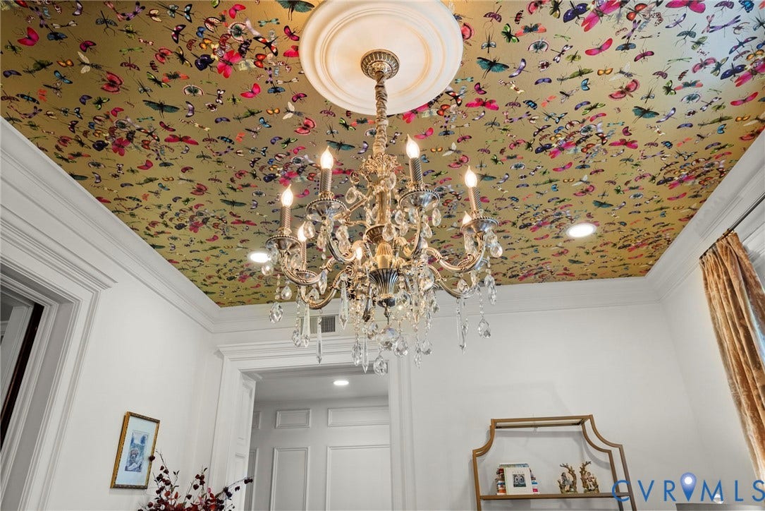 2416 Park Avenue, #U4, The Fan District, Richmond, VA 23220 Intricate multi-arm crystal chandelier suspended from a ceiling medallion, set against a gold-tone ceiling featuring a decorative insect and butterfly motif, complemented by crown molding