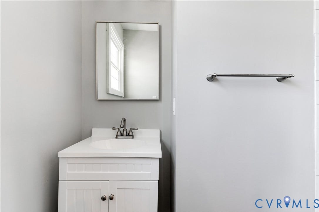620 Chimborazo Boulevard, Church Hill, Richmond, VA 23223 White vanity featuring an integrated countertop, stainless steel dual-handle faucet, rectangular wall-mounted mirror, and horizontal towel bar