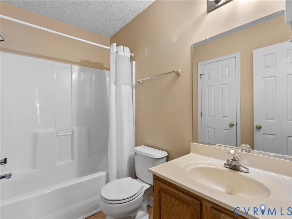 9520 Willow Ridge Drive, Glen Allen, VA 23060 Bathroom featuring a molded composite tub and shower surround, wood-finish vanity with an integrated basin, wall-mounted mirror, and six-panel interior doors