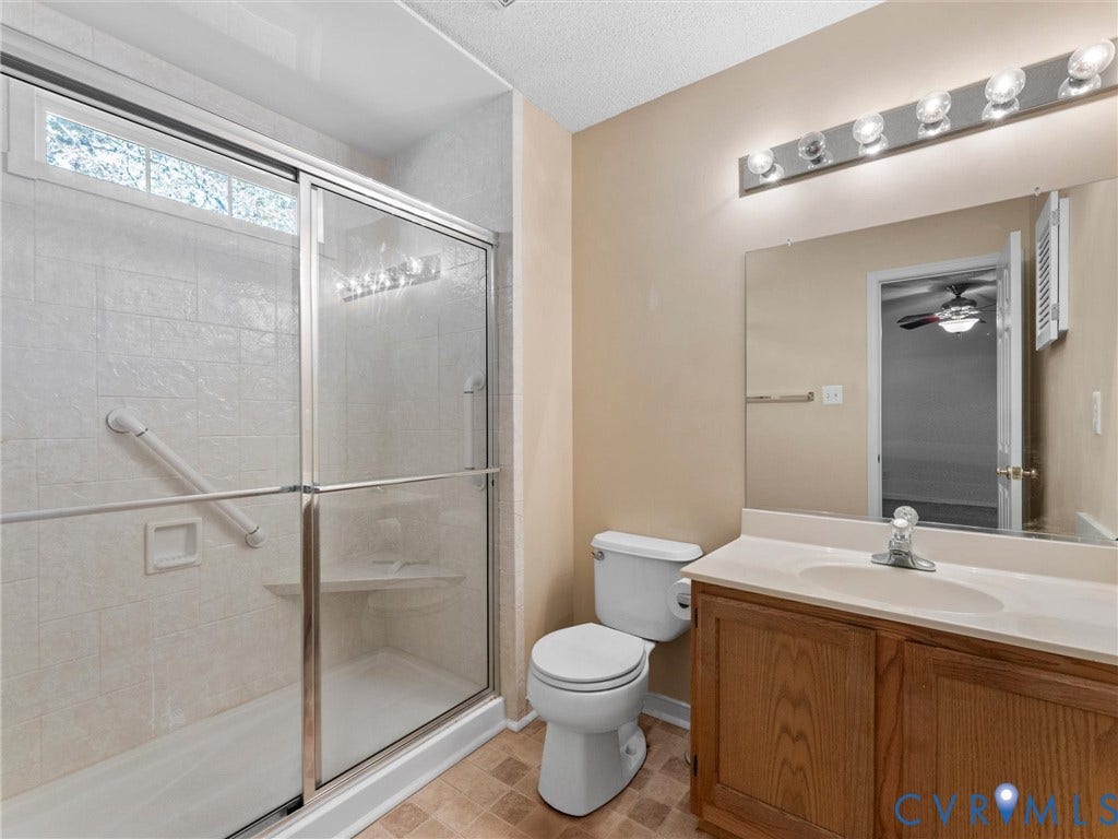 9520 Willow Ridge Drive, Glen Allen, VA 23060 Bathroom featuring a walk-in shower with sliding glass doors, built-in corner bench, and integrated grab bar, complemented by a wood-finish vanity with an oval basin and a large wall-mounted mirror