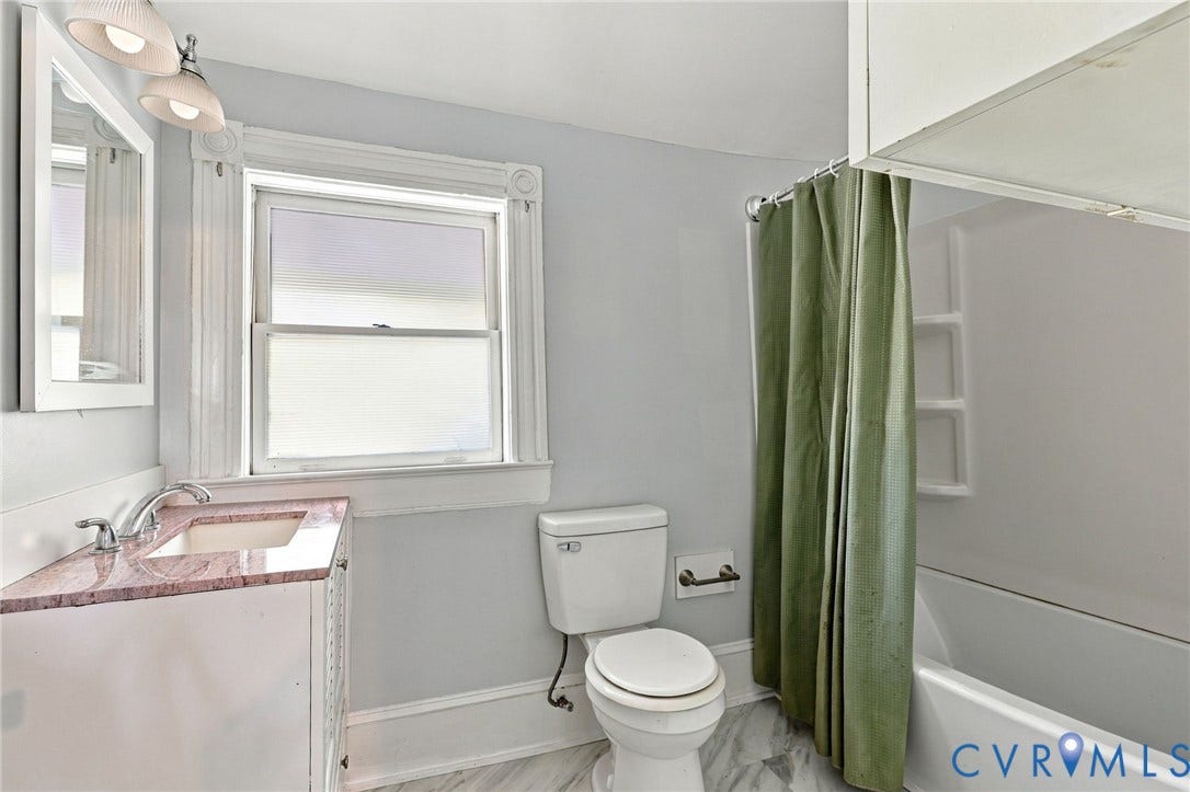 1911 3rd Avenue, Richmond, VA 23222 Bathroom featuring a single-sink vanity with stone countertop, window with decorative trim, and combination tub and shower with integrated shelving