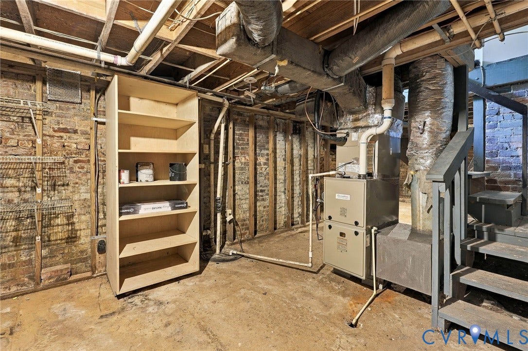 1911 3rd Avenue, Richmond, VA 23222 Unfinished basement area featuring exposed brick walls, concrete flooring, built-in shelving, and a gas furnace