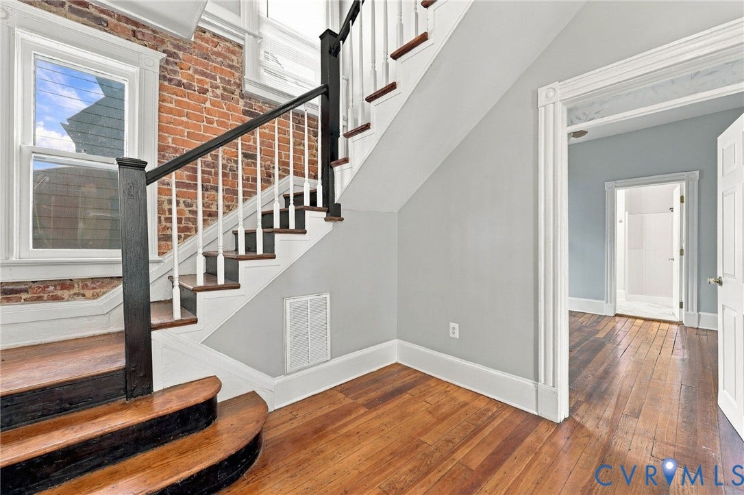 1911 3rd Avenue, Richmond, VA 23222 Exposed brick accent wall, wood-finish flooring, and a staircase featuring wood treads with a dark-finished handrail and white balusters