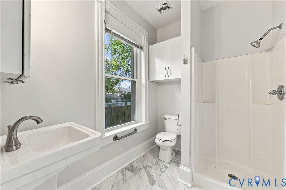1911 3rd Avenue, Richmond, VA 23222 1st floor Bathroom : Wall-mounted pedestal sink with high-arc faucet, tiled stall shower, porcelain toilet, and overhead built-in cabinetry, finished with patterned tile flooring