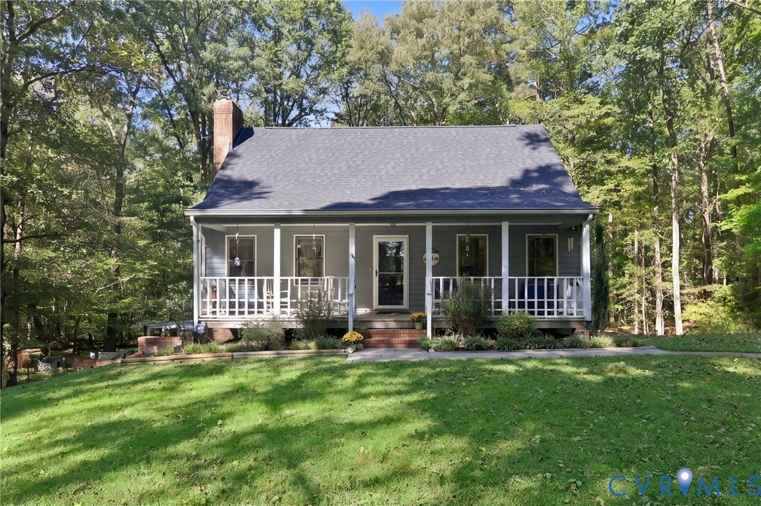 1330 Ruffin Mill Road, South Chesterfield, VA 23834 Cape Cod style exterior featuring a covered front porch with railings, a brick chimney, and a backdrop of mature trees