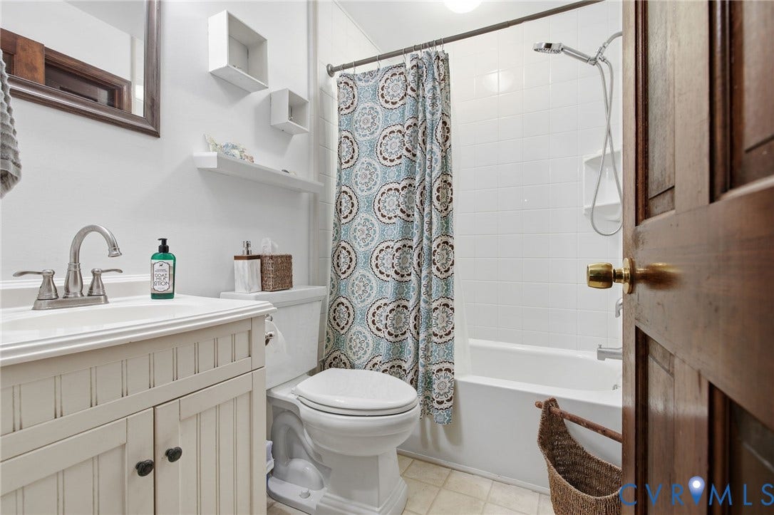 1330 Ruffin Mill Road, South Chesterfield, VA 23834 Bathroom featuring a beadboard vanity cabinet with a solid surface countertop, chrome dual-handle faucet, built-in wall shelving, and a shower-tub combination with white tile surround