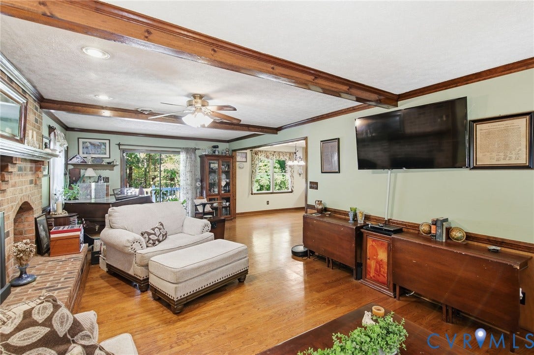 1330 Ruffin Mill Road, South Chesterfield, VA 23834 Living area featuring exposed stained wood ceiling beams, brick fireplace surround, wood-finish flooring, and crown molding
