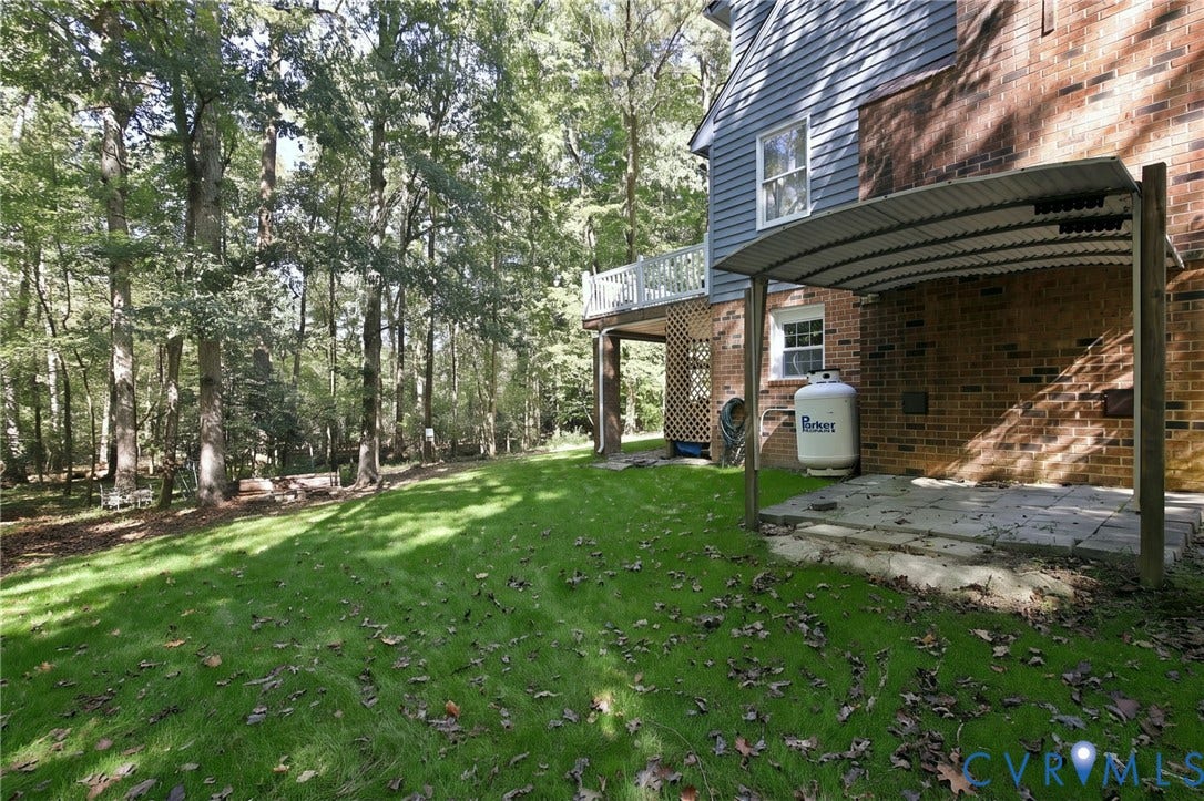 1330 Ruffin Mill Road, South Chesterfield, VA 23834 Backyard featuring a paved patio with a corrugated metal cover, an elevated wood-railing deck, red brick and horizontal siding exterior, and mature trees