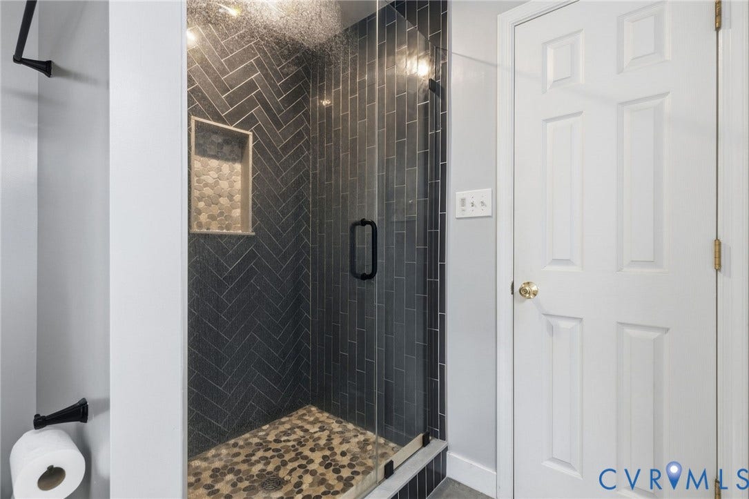 4350 Steger Creek Drive, Powhatan, VA 23139 Walk-in shower featuring dark herringbone tile walls, a built-in recessed niche, pebble-stone flooring, and a frameless glass door with matte black hardware