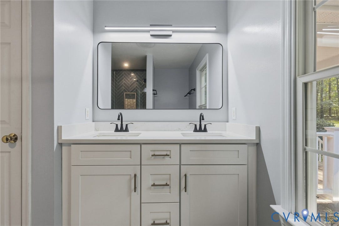 4350 Steger Creek Drive, Powhatan, VA 23139 Dual-vanity cabinetry with a light finish, quartz countertop, rectangular under-mount sinks, matte black hardware, and an elongated linear light fixture